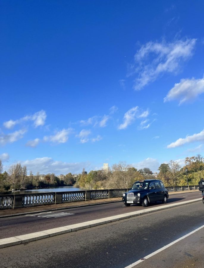 An iconic London black cab crosses a bridge over the river Thames. 