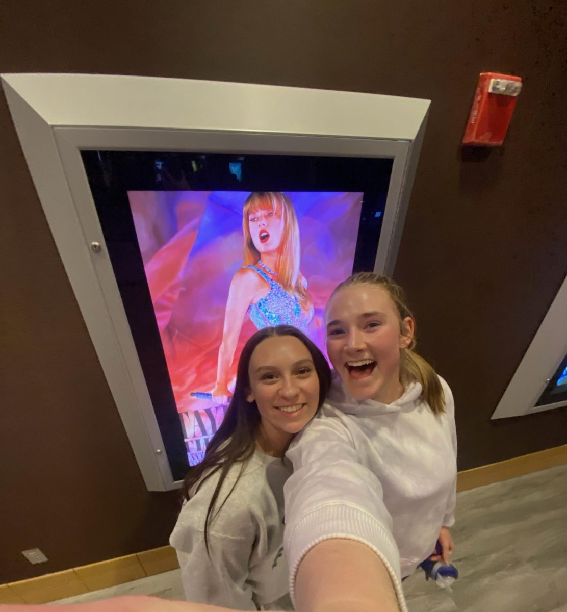My friend Aly and I take a picture with the Taylor Swift: The Eras Tour movie poster. 