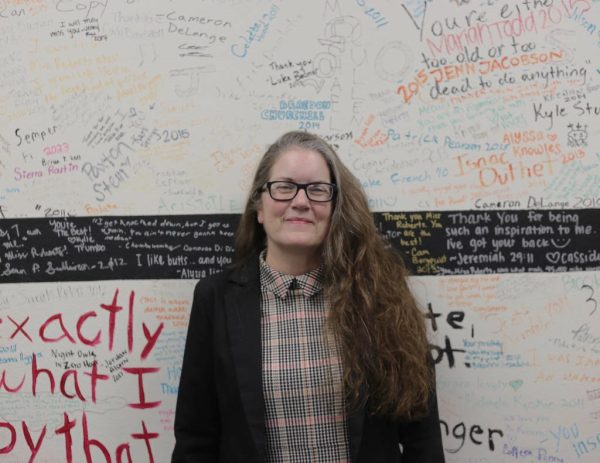Ms. Roberts poses in front of her wall of  former student signatures. 